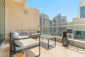 A balcony with a sofa, a table, and a decorative vase. - Business Bay Apartment w Balcony Seating (Dubai)