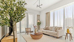A modern living room with a large window, a sofa, a coffee table, and a TV on a wooden stand. - Bright 1BR Escape w Balcony Building Pool (Dubai)