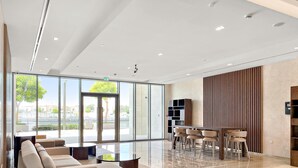 A spacious lobby with a modern sofa, a dining area with chairs, and a large glass door leading outside. - Bright 1BR Escape w Balcony Building Pool (Dubai)