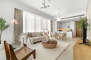Uma sala moderna com sofá, mesa de centro e cadeiras, uma área de jantar com mesa e cadeiras, e uma cozinha ao fundo.