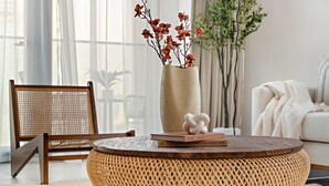 A round woven coffee table with a vase of dried flowers and books on top. - Bright 1BR Escape w Balcony Building Pool (Dubai)