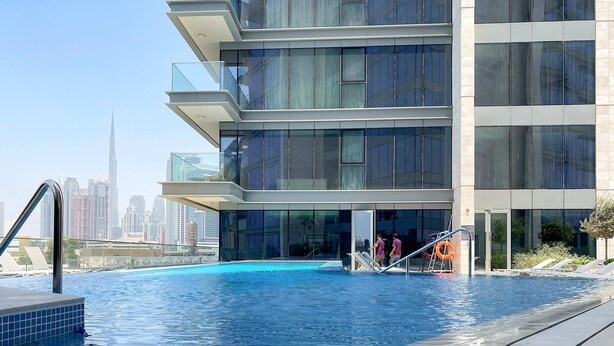 A modern building with a swimming pool, glass balconies, and a city skyline in the background. - Bright 1BR Escape w Balcony Building Pool (Dubai)