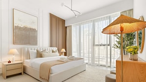 A modern bedroom with a large bed, bedside tables, a wooden nightstand, a floor lamp, and a view of the city through large windows. - Bright 1BR Escape w Balcony Building Pool (Dubai)
