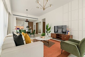 Un salon moderne avec un canapé, une table basse et un téléviseur. On aperçoit à l’arrière-plan un coin repas et une cuisine.