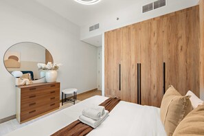 A modern bedroom with a wooden wardrobe, a round mirror, a bedside table with a vase, and a neatly made bed. - Silkhaus Signature 1bdr Apartment in Maryah Island (Abu Dhabi)