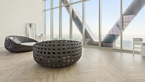 Ein modernes Interieur mit großen Fenstern, Holzboden und zwei Sitzbereichen mit gewebten Möbeln.