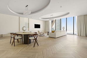 A spacious living area with a modern herringbone floor, a round dining table with chairs, a white sofa, and a large window offering a city view. - Silkhaus 64floor PH Ballroom Hall Private Pool (Abu Dhabi)
