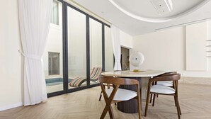 Ein stilvoller Essbereich mit einem runden Tisch und Holzstühlen, großen Fenstern mit Vorhängen und Blick auf einen Pool.