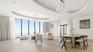 Ein geräumiges Wohnzimmer mit großem Fenster, einem weißen Sofa, einem Esstisch mit Stühlen und einem modernen Deckenstil.