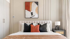 A hotel room with a large bed, a headboard, a bedside table with a lamp, and a wall-mounted abstract painting. - Silkhaus Luxurious 3BR Maid Dubai Hills (Dubai)