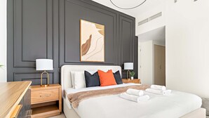 A modern hotel room with a large bed, two bedside tables with lamps, a headboard with a decorative panel, and a view of the hallway. - Silkhaus Luxurious 3BR Maid Dubai Hills (Dubai)