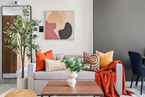 Ein modernes Wohnzimmer mit grauem Sofa, bunten Kissen, einem Holztisch und einer Topfpflanze.