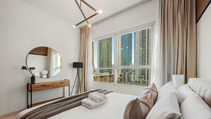 A modern hotel room with a large bed, a bedside table with a mirror, a lamp, and a view of tall buildings through the window. - Silkhaus 3BR Maid Room in Marina Heights Tower (Abu Dhabi)