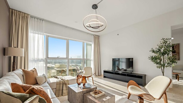 A modern living room with a sofa, coffee table, and armchair, a flat-screen TV, and a large window with a city view. - Silkhaus 3BR Maid Room in Marina Heights Tower (Abu Dhabi)