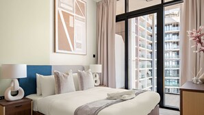 A modern hotel room with a large bed, two bedside tables with lamps, a view of a building through a glass door, and a large framed artwork on the wall. - Silkhaus 1bdr Prime Location in Maryah Island (Abu Dhabi)