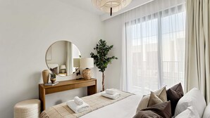 Een moderne hotelkamer met een groot bed, een houten nachtkastje, een ronde spiegel en een kamerplant.