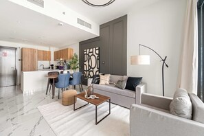 A modern living room with a sofa, armchair, and coffee table. There is a kitchen area with wooden cabinets and a dining table with chairs. - Silkhaus New 1bdr Living in Maryah Island (Abu Dhabi)