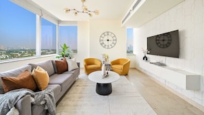 Ein modernes Wohnzimmer mit einer Couch, zwei Sesseln, einem Couchtisch und einem an der Wand montierten Fernseher.
