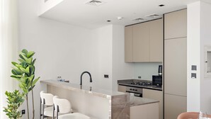 A modern kitchen with a central island, bar stools, and a dining table with chairs. - Silkhaus Elite 1bdr Business Bay High Floor (Dubai)