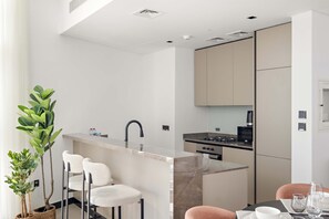 A modern kitchen with a central island, bar stools, and a dining table with chairs. - Silkhaus Elite 1bdr Business Bay High Floor (Dubai)