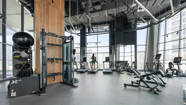 A gym with cardio machines, weightlifting equipment, and a large mirror. - Silkhaus Elite 1bdr Business Bay High Floor (Dubai)