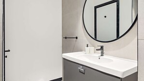 A modern bathroom with a white sink, a round mirror, and a door. - Silkhaus Elite 1bdr Business Bay High Floor (Dubai)