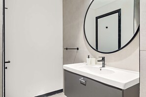 A modern bathroom with a white sink, a round mirror, and a door. - Silkhaus Elite 1bdr Business Bay High Floor (Dubai)