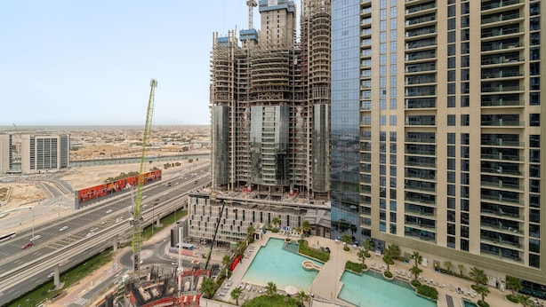 A high-rise building under construction with a swimming pool and a view of the surrounding cityscape. - Silkhaus Cozy Studio High Floor Business Bay (Dubai)