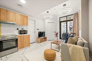 A modern kitchen with wooden cabinets, a built-in oven, and a microwave. There is a dining area with a sofa and a coffee table. - Silkhaus Bright Cozy 1bdr in Al Maryah Vista (Abu Dhabi)