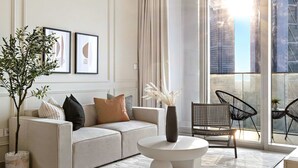 A modern living room with a sofa, coffee table, and chairs, large windows with a city view, and a hanging light fixture. - Silkhaus Modern 1 BDR Forte Tower Downtown (Dubai)