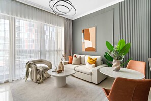 Uma sala de estar moderna com um sofá, mesa de centro e cadeiras, uma janela grande com cortinas e uma planta sobre uma mesinha.