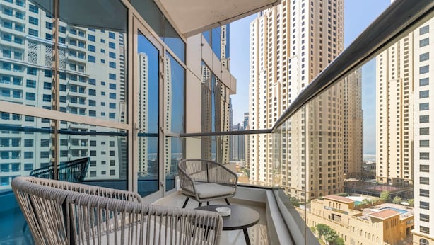 A balcony with wicker furniture and a view of tall buildings. - Silkhaus Modern 1BR Dubai Marina Bay Central (Dubai)
