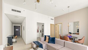 A modern living room with a beige sofa, a round coffee table, and a dining area with a table and chairs. - Silkhaus Urban Chic 1bdr Heart of Downtown (Dubai)