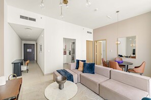 A modern living room with a beige sofa, a round coffee table, and a dining area with a table and chairs. - Silkhaus Urban Chic 1bdr Heart of Downtown (Dubai)