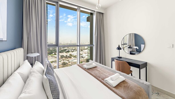 A modern hotel room with a large bed, a wooden side table, a desk, and a large window offering a city view. - Silkhaus Urban Chic 1bdr Heart of Downtown (Dubai)