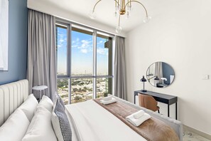 A modern hotel room with a large bed, a wooden side table, a desk, and a large window offering a city view. - Silkhaus Urban Chic 1bdr Heart of Downtown (Dubai)