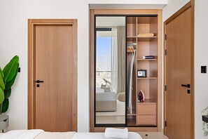 Ein Hotelzimmer mit einem Holzschrank, einer Glastür mit Schieberegler, die auf einen Balkon führt, und einem Bett mit weißer Bettdecke.