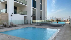 A rooftop pool area with a large pool, lounge chairs, and a city skyline view. - Silkhaus Elite 1bdr in JVC Summer Promotion (Dubai)