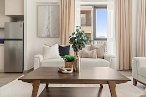 A modern living room with a wooden coffee table, a refrigerator, a sofa with cushions, and a potted plant. - Silkhaus Chic 1BR Creek Beach Grove Pool View (Dubai)
