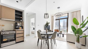 Eine moderne Küche mit Einbauherd, ein Essbereich mit rundem Tisch und Stühlen sowie ein großes Fenster mit Blick auf die Stadt.