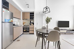 A modern kitchen with a built-in oven, a dining area with a round table and chairs, and a flat-screen TV mounted on the wall. - Silkhaus Stylish 1BR Pool Gym Burj Crown (Dubai)