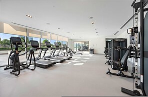 A modern gym with treadmills, weight machines, and large windows offering views of the outdoors. - Silkhaus Stylish 1BR Pool Gym Burj Crown (Dubai)