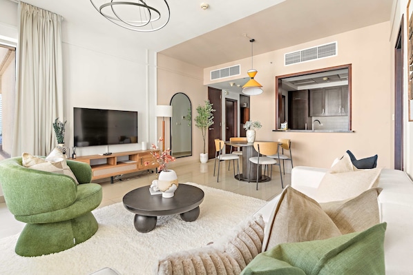 A modern living room with a flat-screen TV, green armchairs, a round coffee table, and a dining area with a table and chairs. - Silkhaus Elite 1bdr at 29 Boulevard Downtown (Dubai)