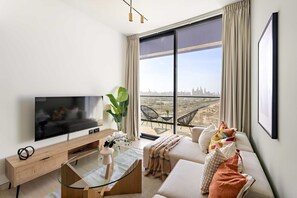 Ein modernes Wohnzimmer mit einem großen Flachbildfernseher, einem Glastisch, einer Couch mit Kissen und Blick auf eine Stadtlandschaft durch große Fenster.