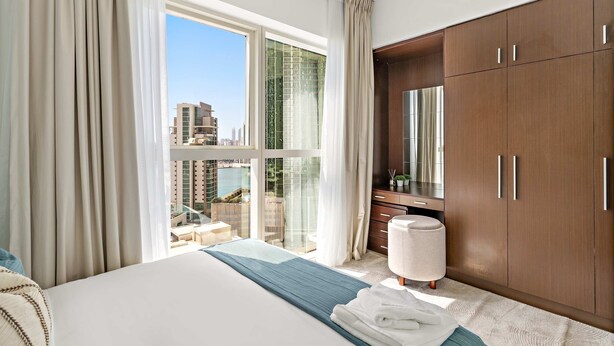 Quarto de hotel com uma cama grande, um guarda-roupa, uma casa de banho com porta de vidro e vista para a cidade.
