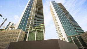 Dois arranha-céus altos e modernos com fachadas de vidro refletivo, rodeados por outros edifícios.