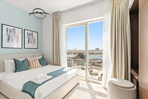 Ein modernes Hotelzimmer mit einem großen Bett, zwei gerahmten Kunstwerken, Blick auf eine Marina und einem Balkon mit Stadtblick.