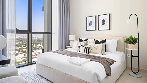 Ein modernes Hotelzimmer mit einem großen Bett, Blick auf die Stadt und einer Topfpflanze.