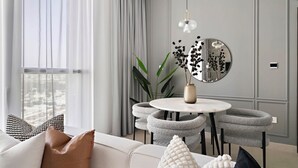 Ein modernes Wohnzimmer mit einem runden Esstisch, grau gepolsterten Stühlen, einem weißen Sofa und einem großen Spiegel an der Wand.