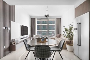 Ein modernes Wohnzimmer mit einem runden Esstisch, schwarzen Stühlen, einer Couch, einem Fernseher und einem großen Fenster mit Vorhängen.